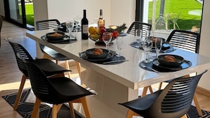 Et moderne spiseområde med et langt bord, sorte stole og udsigt til en grøn græsplæne.
