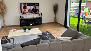 En moderne stue med en stor, grå modulsofa, et hvidt sofabord og et fladskærms-tv monteret på væggen.