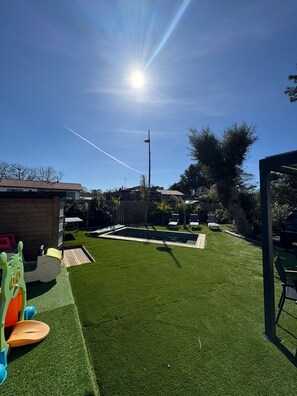 Un jardin avec une pelouse artificielle, une piscine et un espace de jeux.