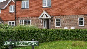 A traditional brick cottage with a white door and multiple windows, surrounded by a well-maintained hedge and a sign reading "Crown Cottages". - 3 bedroom accommodation in Horsted Keynes (Horsted Keynes)