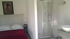 Una camera da letto con un letto, un comodino con un vaso e un angolo doccia con un lavandino.