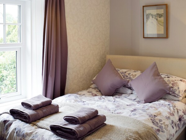 Una cama bien hecha con un edredón estampado con motivos florales, dos almohadas y una manta doblada.