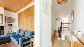 A living room with a blue sofa, wooden paneling, a staircase, and a dining area with a wooden table and chairs. - Cyrus House Dartford Centre (Dartford)
