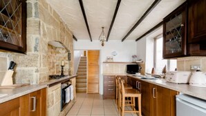 A kitchen with stone walls, wooden cabinets, a central island with stools, and a staircase leading to another room. - Cyrus House Dartford Centre (Dartford)