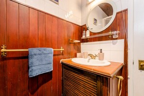 A bathroom with wooden paneling, a round mirror, a sink with a gold faucet, and a towel rack. - Cyrus House Dartford Centre (Dartford)