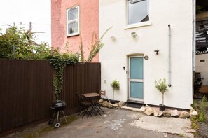 A two-story house with a white exterior, a blue door, and a small garden area with a table and chairs. - Cyrus House Dartford Centre (Dartford)