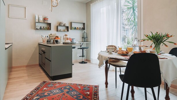 A modern kitchen with a central island, dining area with chairs, and a view of a garden through large windows.