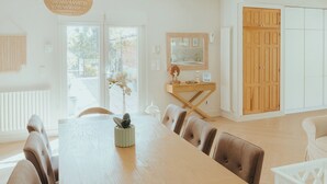 A modern dining area with a wooden table and chairs, a hanging light fixture, and a view of the outdoors through a glass door.