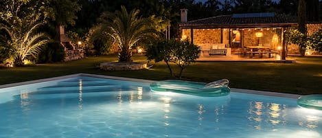 A swimming pool with clear water, surrounded by a well-lit patio area with outdoor furniture.