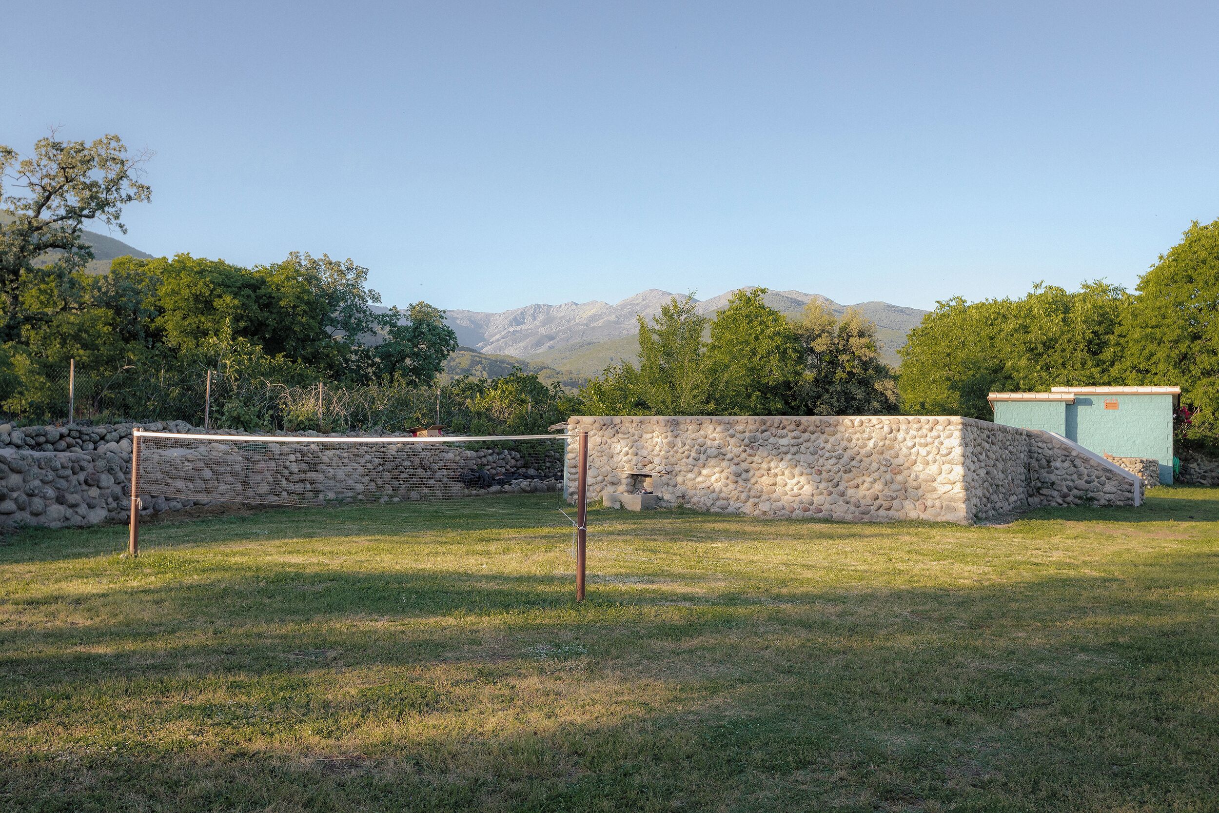 A grassy area with a volleyball net, stone wall, and a small building.