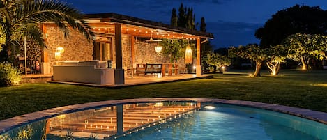 Una piscina con zona de patio, paredes de piedra y mobiliario exterior.