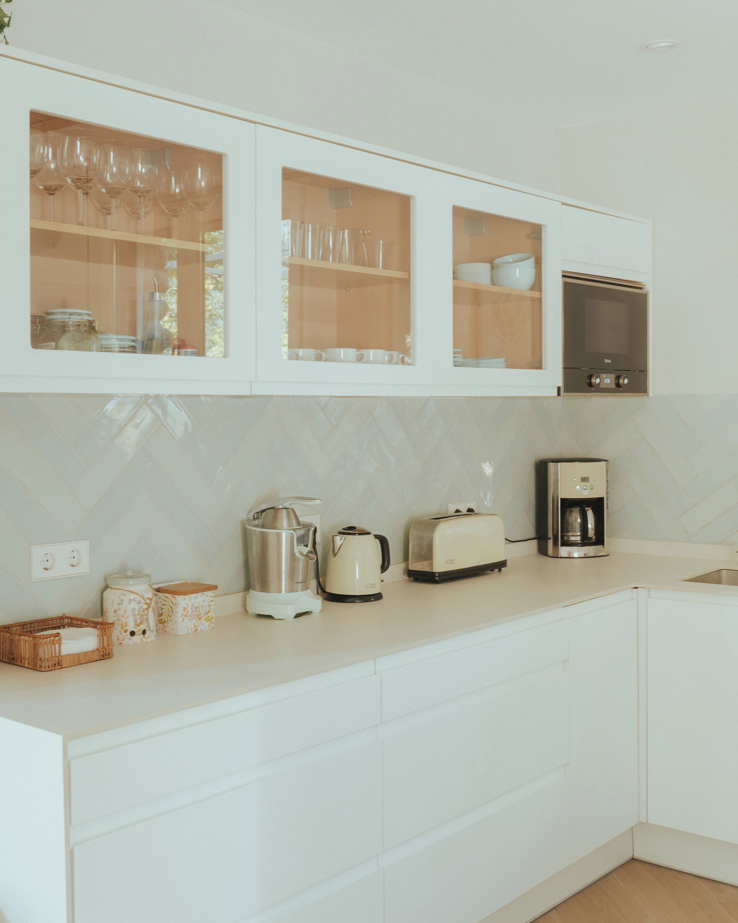 A modern kitchen with white cabinetry, a built-in oven, and various appliances including a coffee maker and toaster.