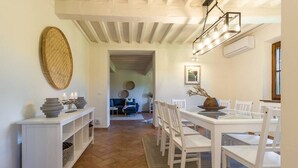 Un coin repas avec une table et des chaises blanches, un panier tressé accroché au mur et un luminaire au plafond.