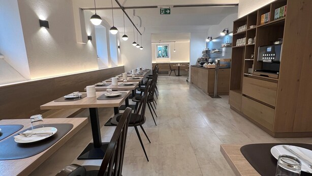 A modern restaurant with long tables, black chairs, and pendant lighting. - Villa Flöckner (Salzburg)