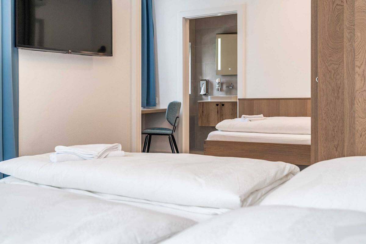 A hotel room with a bed, a desk with a chair, a TV, and a bathroom with a mirror and sink.