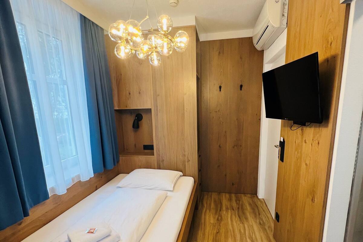A hotel room with a wooden bed, a TV mounted on the wall, and a wooden floor.