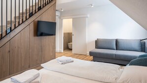 A modern living room with a grey sofa, a flat-screen TV mounted on a wooden wall, and a staircase leading to an upper level. - Villa Flöckner (Salzburg)
