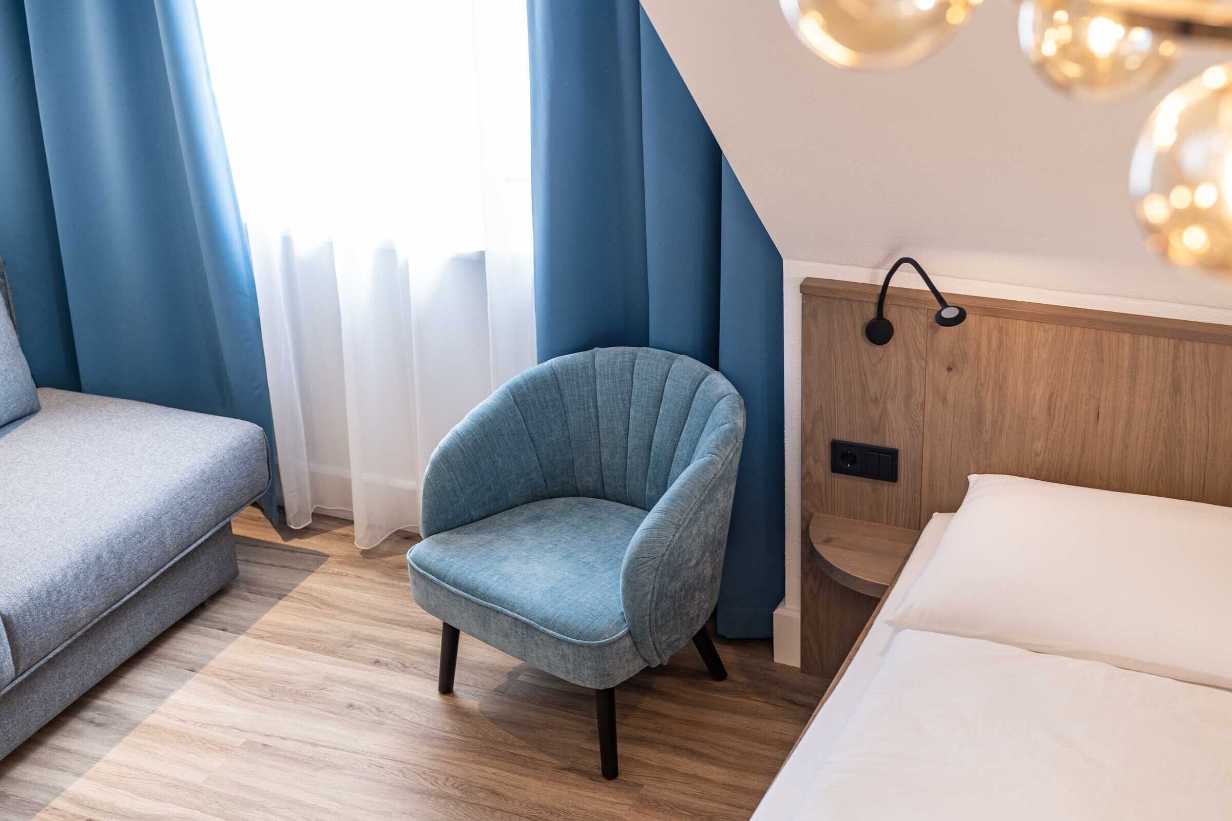Une chambre moderne avec un fauteuil bleu, un canapé et un lit.