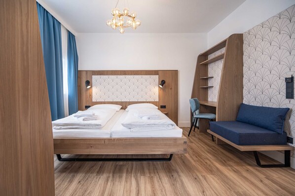 A modern hotel room with a wooden bed, a blue sofa, and a built-in bookshelf.
