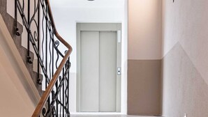 A staircase with a wooden handrail and black metal balusters leading to a door with a light switch above it. - Villa Flöckner (Salzburg)