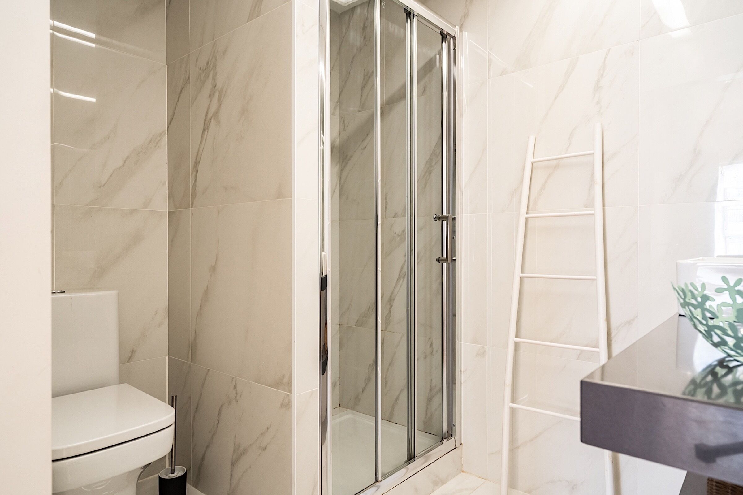 A bathroom with a glass-enclosed shower, a toilet, and a white tiled wall.