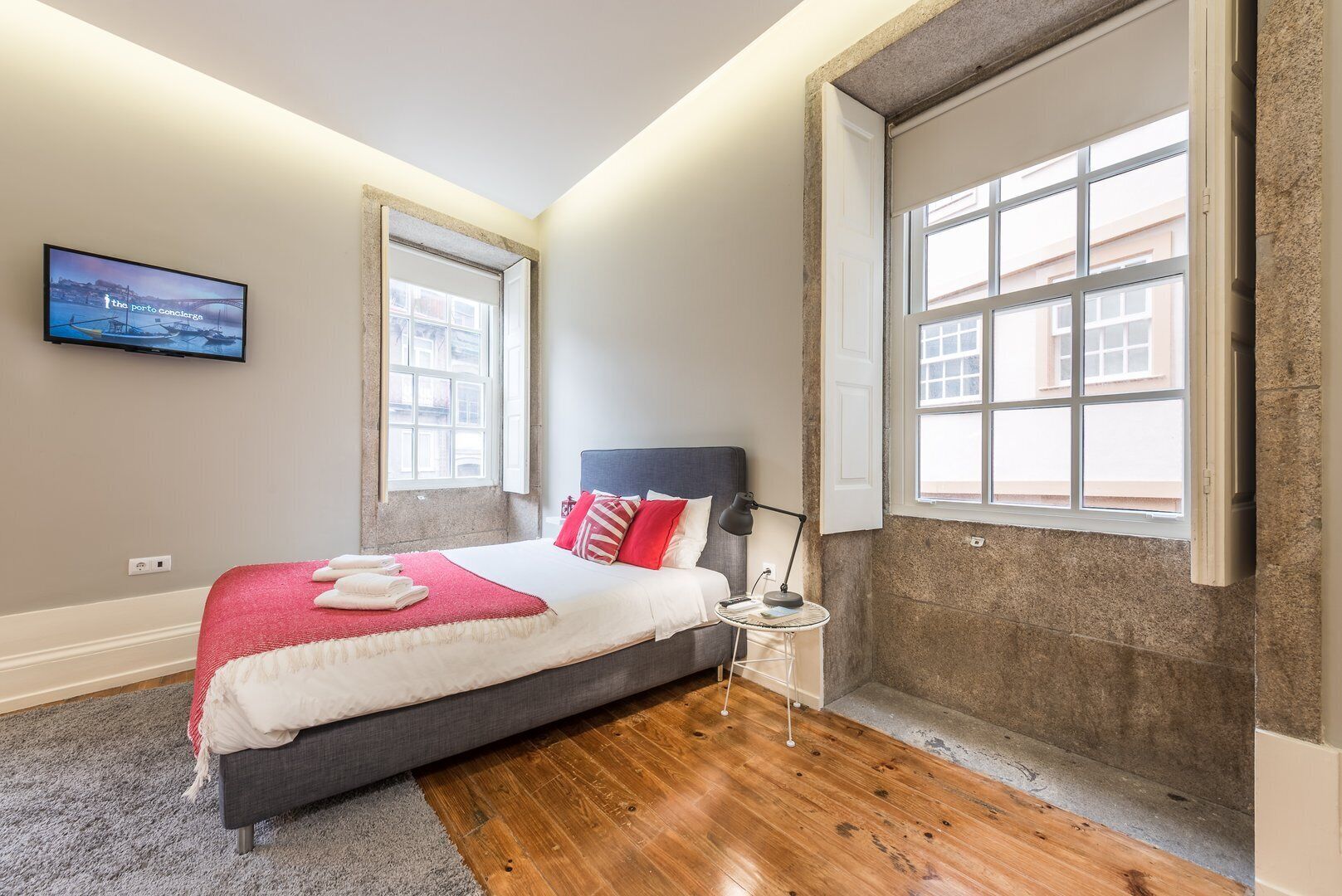 A bedroom with a bed, a TV, a nightstand, and a large window.