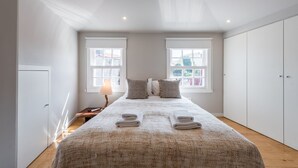 A bedroom with a bed, two windows, a bedside table with a lamp, and a wardrobe. - GuestReady - Modern luxe getaway in Vitória (Porto)