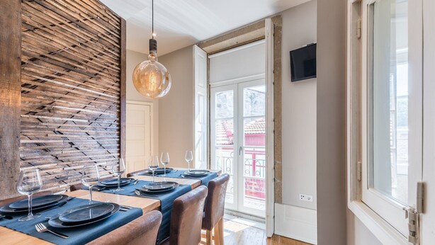 A dining area with a wooden wall, a hanging light fixture, and a view of a red building outside. - GuestReady - Modern luxe getaway in Vitória (Porto)