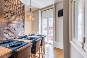Un comedor con pared de madera, una lámpara colgante y vista a un edificio rojo en el exterior.