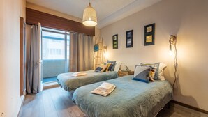 Camera d'albergo con due letti, un'ampia finestra con tende, un lampadario e quadri appesi alle pareti.