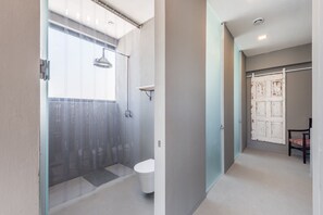 A modern bathroom with a glass shower enclosure, a white toilet, and a wooden door with a distressed finish. - GuestReady - Sunset Pool House (Esposende)