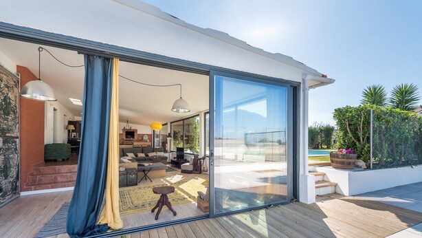 A modern house with a large sliding glass door leading to a spacious living area and a pool. - GuestReady - Sunset Pool House (Esposende)