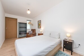 A bedroom with a bed, a wardrobe, a chair, a nightstand, and a lamp. - GuestReady - Sunset Pool House (Esposende)
