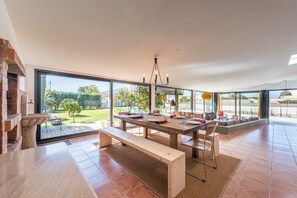 A spacious dining area with a large table, benches, and a view of the outdoors. - GuestReady - Sunset Pool House (Esposende)