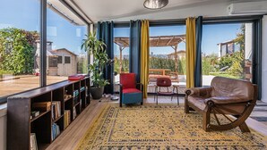 A spacious living room with large windows, a red chair, a brown leather sofa, and a bookshelf. - GuestReady - Sunset Pool House (Esposende)