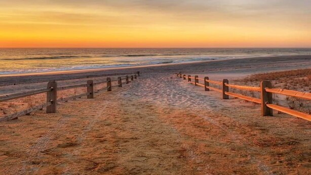 Une plage bordée d’une clôture en bois et d’une promenade qui mène à l’océan.