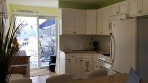Une cuisine avec des armoires blanches, une cuisinière et un réfrigérateur. Il y a une affiche sur le mur qui porte l’inscription : « Pourquoi limiter le bonheur à une heure ? »