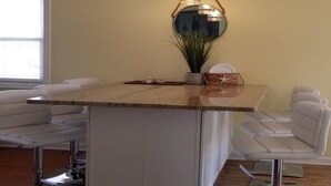 Une cuisine moderne avec un plan de travail en marbre, des tabourets de bar blancs et des luminaires suspendus.
