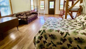 Une chambre avec un lit en bois, un canapé, un bureau et une échelle menant à une mezzanine.