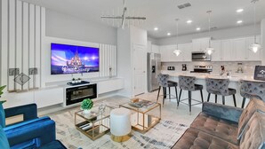 Uma sala de estar moderna com televisão de tela plana, um sofá, uma mesa de centro e um espaço de cozinha com banquetas.