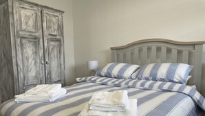 Una cama bien hecha con ropa de cama a rayas y toallas dobladas, un cabecero de madera y un armario grande.