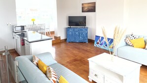 Una sala de estar moderna con un sofá, una mesa de centro, un televisor y una cocina con microondas.