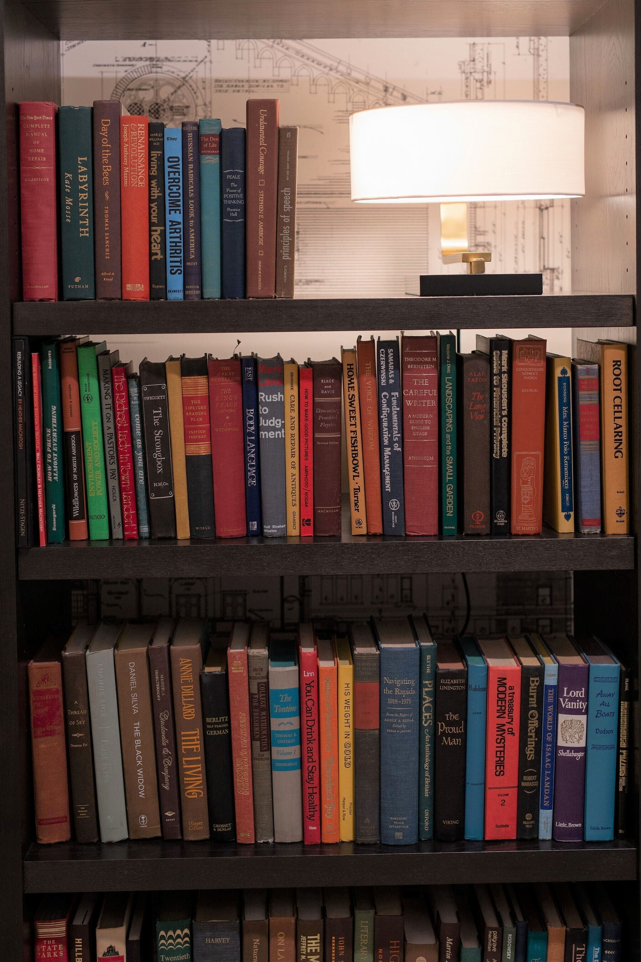Une bibliothèque remplie de divers ouvrages, une lampe et un décor composé de plans d’architecture.
