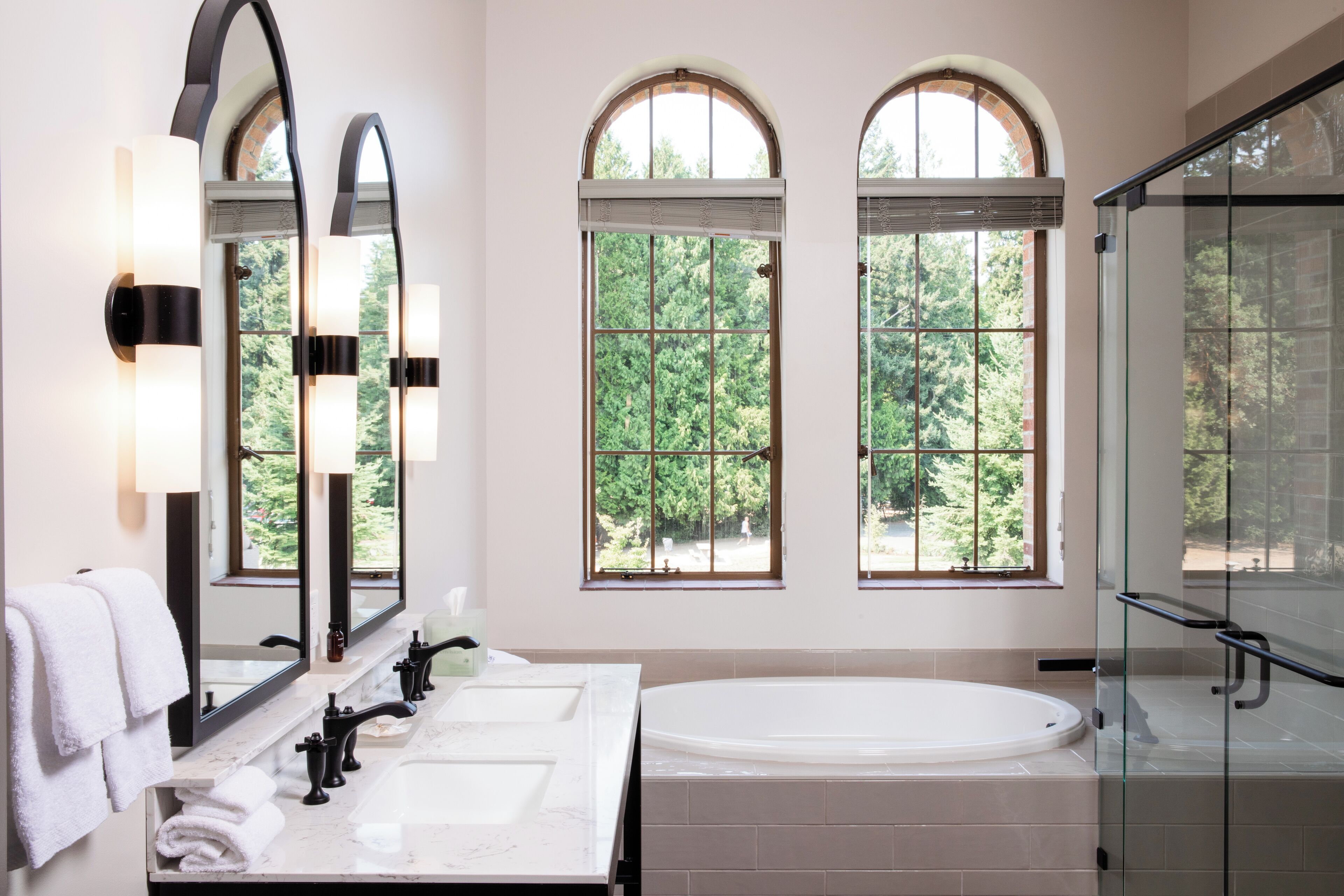 A bathroom with two sinks, a large bathtub, and three windows with arched tops.