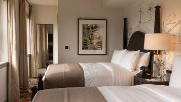 A hotel room with two beds, a large framed botanical print on the wall, a nightstand with a lamp, and a mirror.