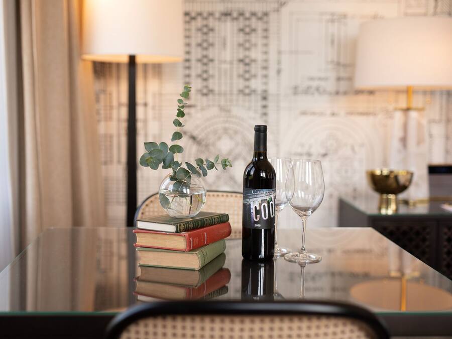 A glass table with a bottle of wine, a glass, and a vase with a plant. There are books stacked on the table.