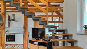 Une cuisine moderne dotée d’un four encastré et d’une cuisinière, d’un escalier en bois et d’un téléviseur posé sur un meuble en bois.