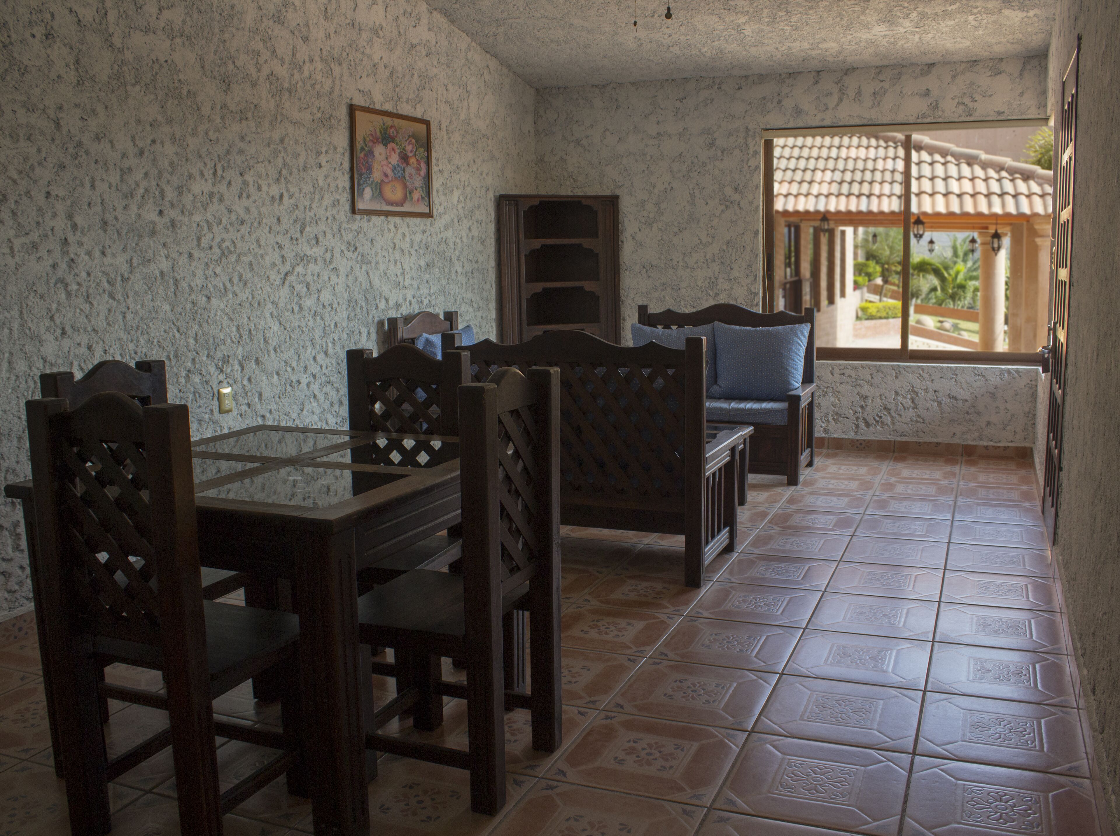 Un comedor con mesa y sillas de madera, pared con diseño y ventana con vistas a vegetación.