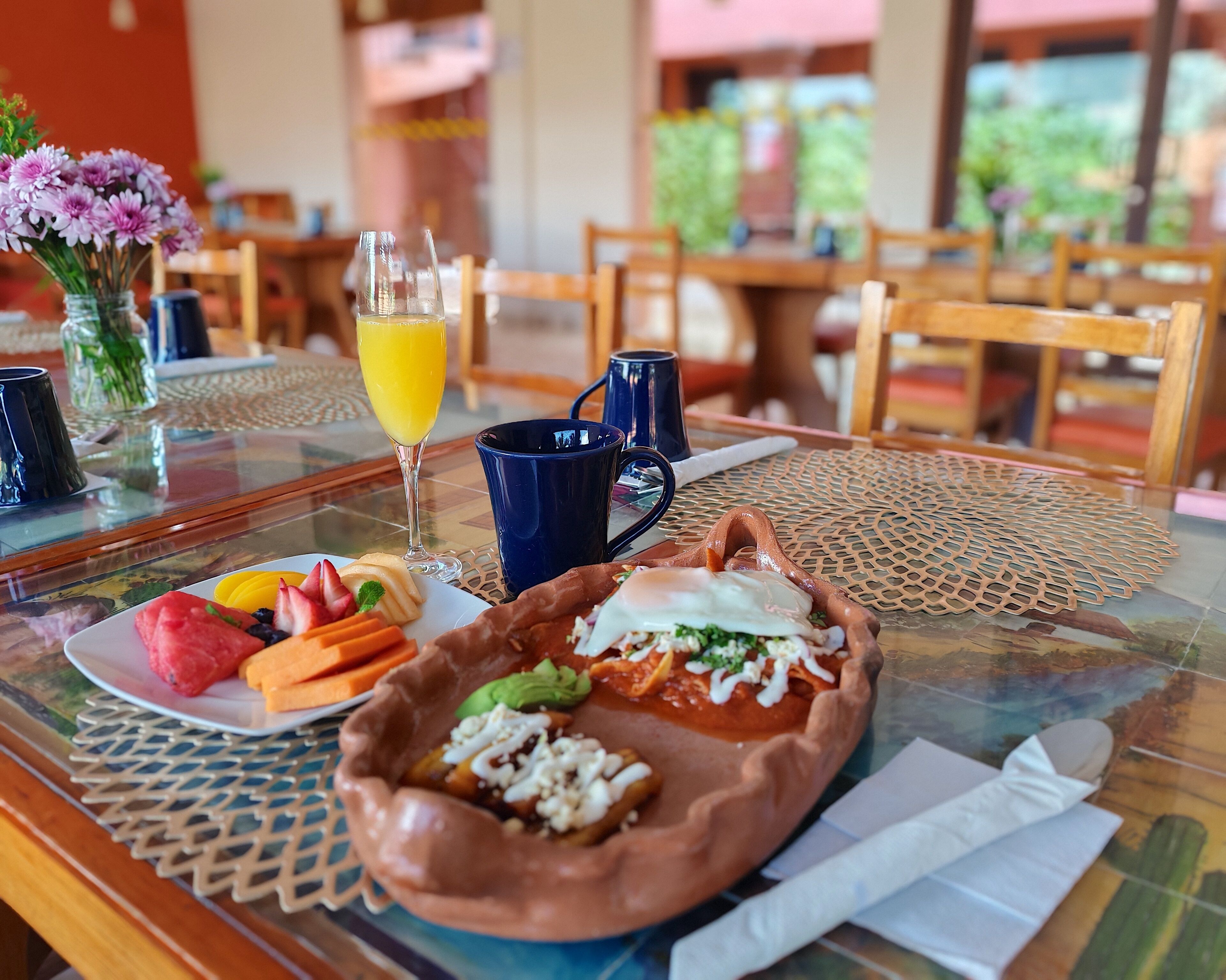 A breakfast table with a plate of food, a glass of orange juice, and a blue mug.