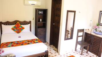 A hotel room with a bed, a wooden wardrobe, a desk with a chair, and a mirror on the wall.